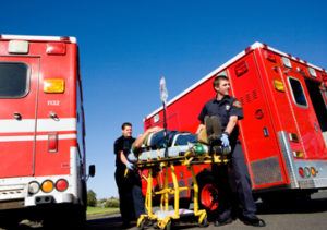 Two paramedics wheeling a patient on a gurney between two ambulances.