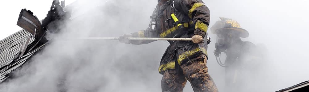 two firefighters on rooftop fighting an active fire