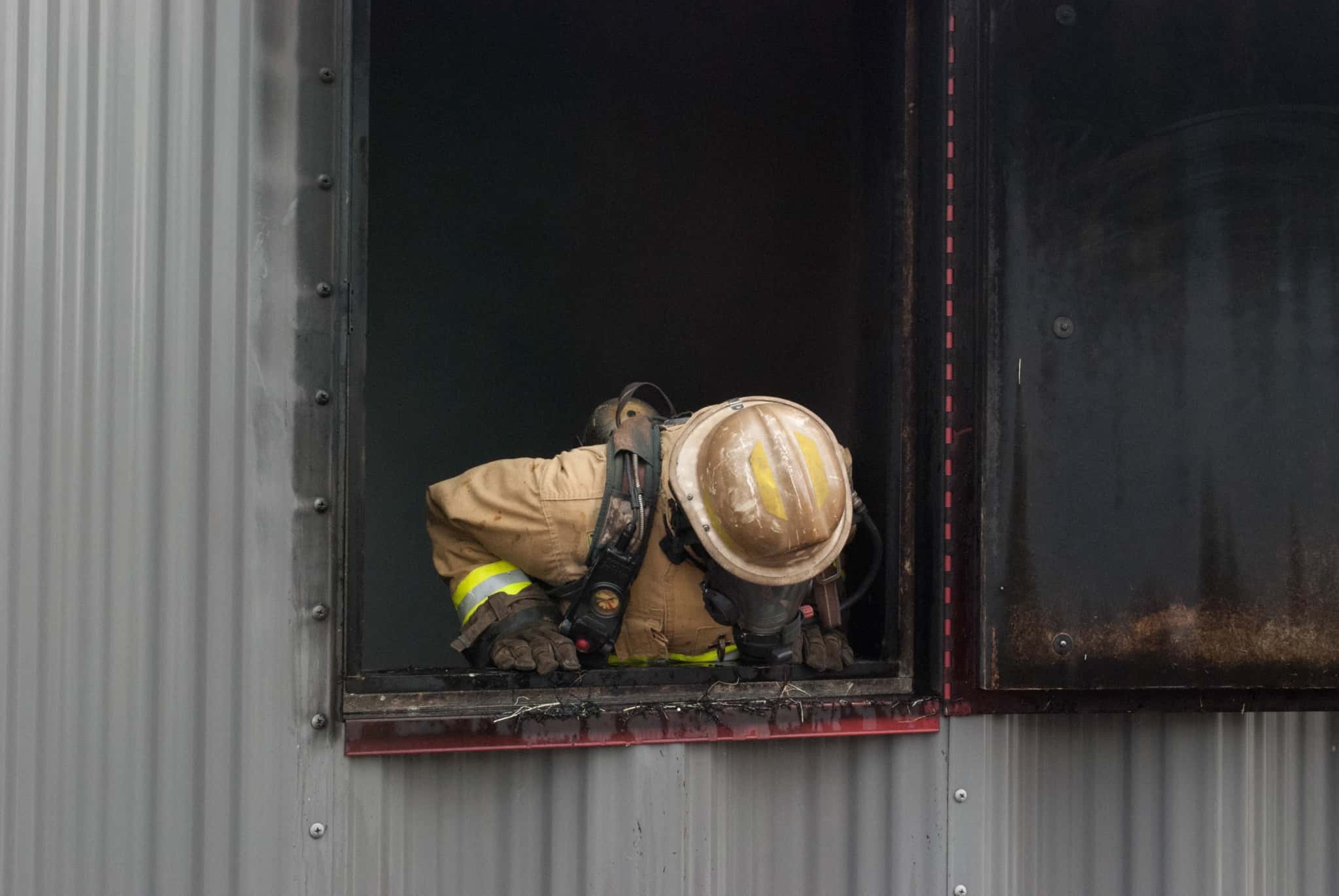 Firefighter looks down out of a charred window.