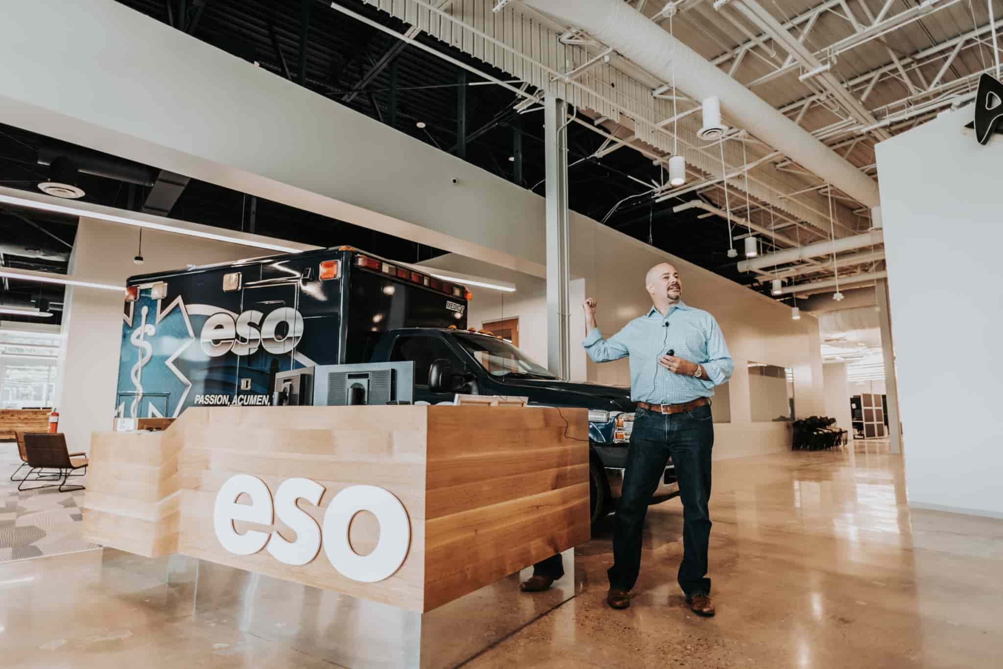 A man speaking in front of an ESO branded ambulance during a happy hour event.