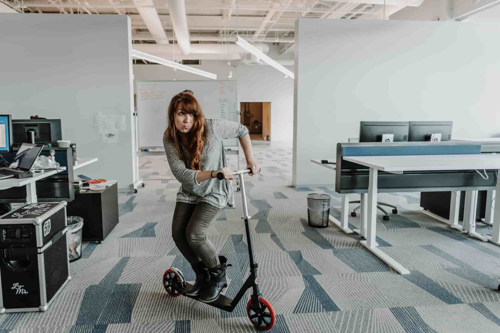 A woman riding a scooter in an office.