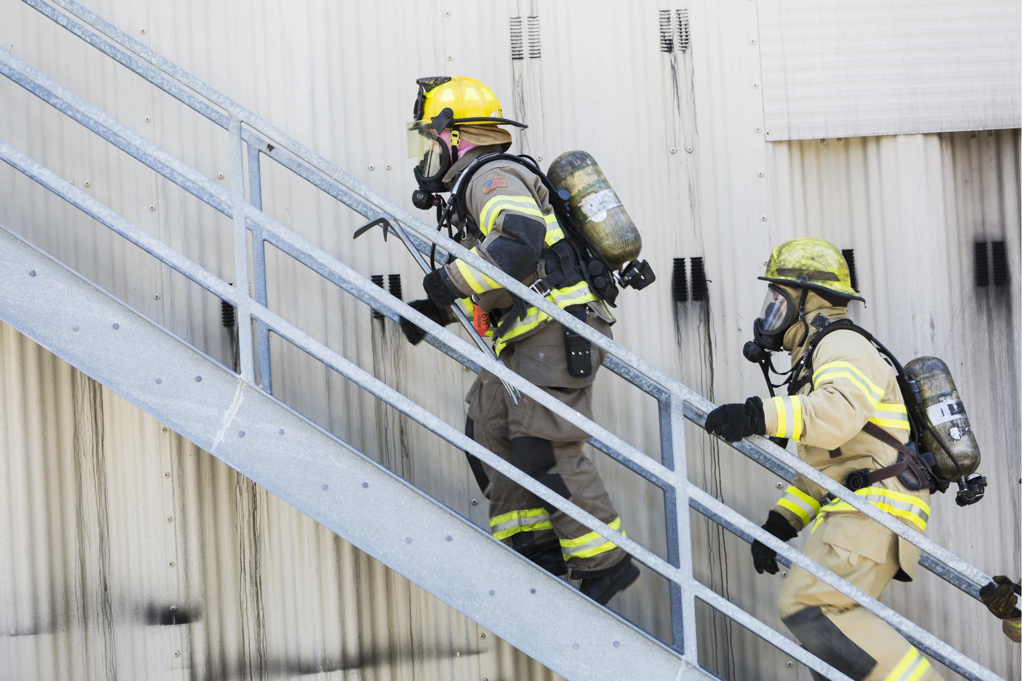 Two firefighters in protective gear climbing stairs
