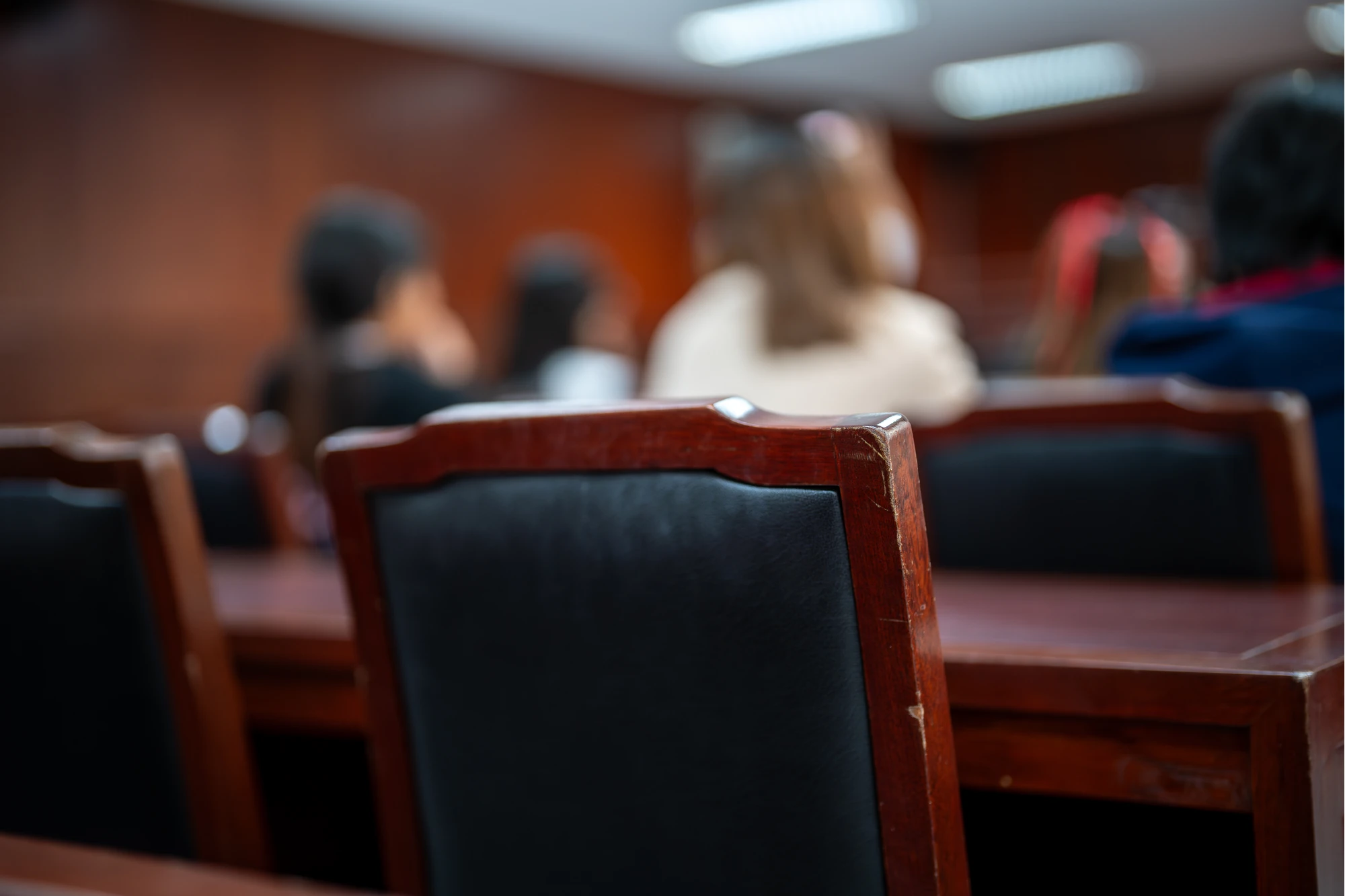 A group of people are sitting in a room with wooden chairs