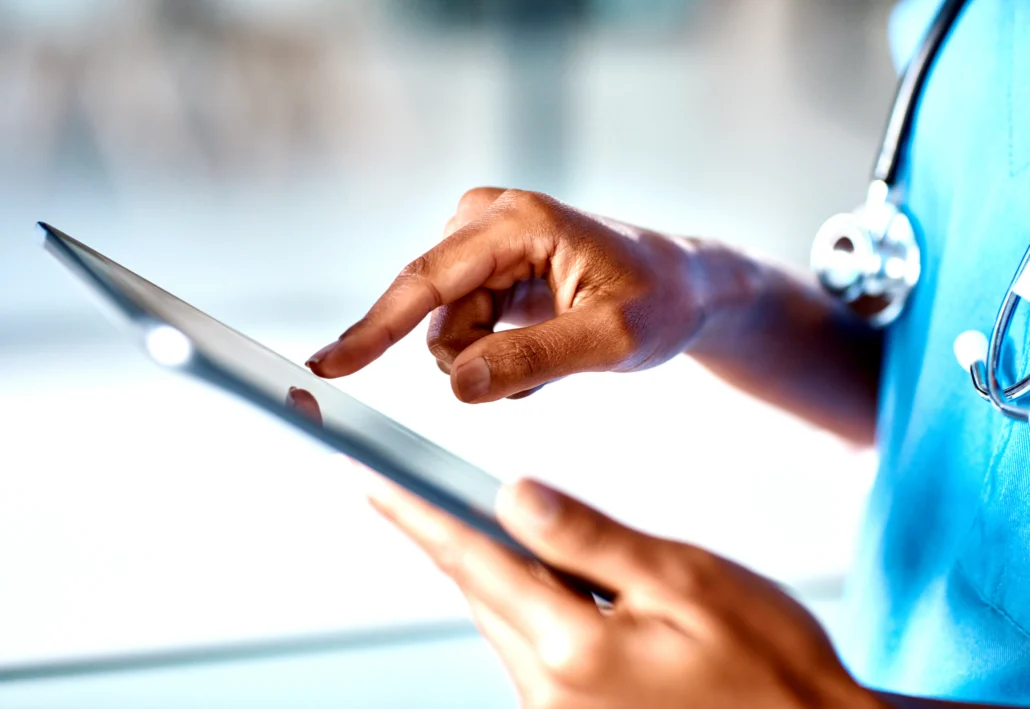 A healthcare professional in blue scrubs with a stethoscope uses a digital tablet.